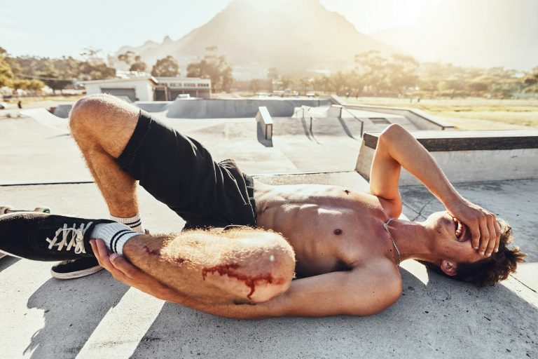 Injury, blood and knee with a topless man crying in agony after a fall or accident to damage his bo